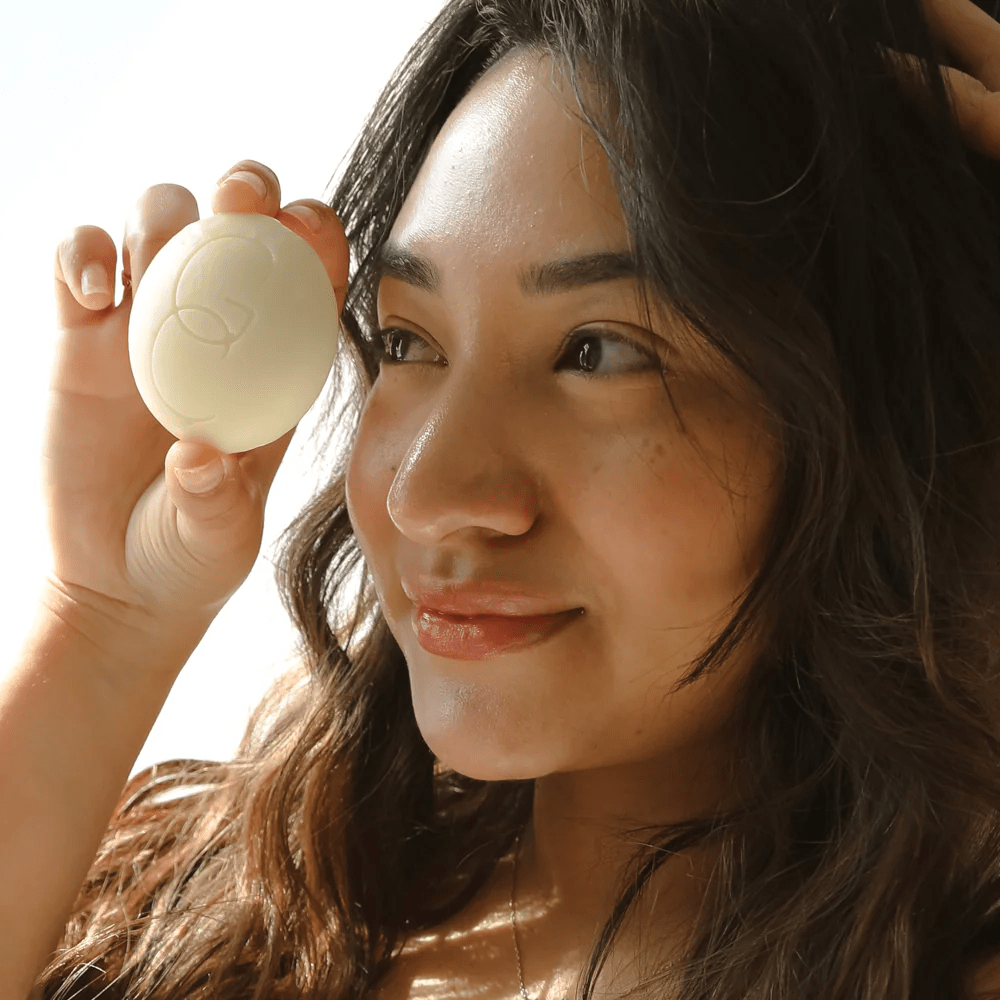 A woman with long dark hair holds a Good Condition lotion bar to her face.